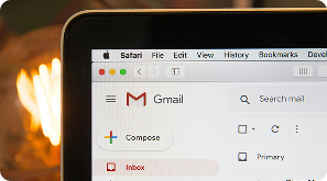 A close-up of a laptop screen displaying the Gmail inbox in a web browser, with the Compose button visible on the left sidebar and blurred background lighting.