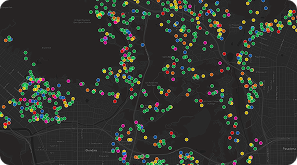 A dark map displays clusters of multicolored dots scattered across a city area, indicating various data points or locations. Major roads and some neighborhoods are faintly visible beneath the colored markers.