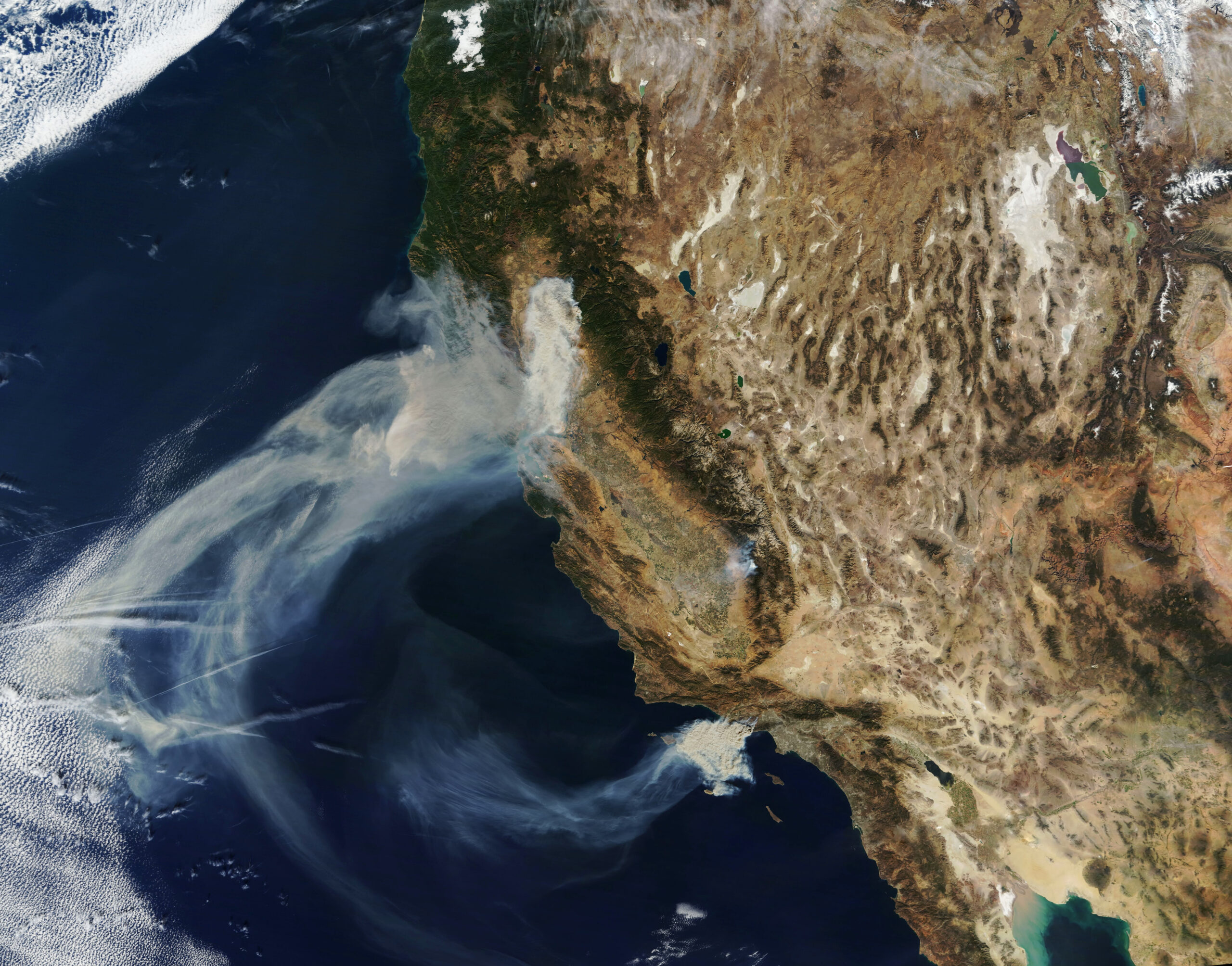 Satellite view of the western United States showing thick smoke from wildfires drifting over California and into the Pacific Ocean, with parts of Oregon, Nevada, and Mexico also visible.
