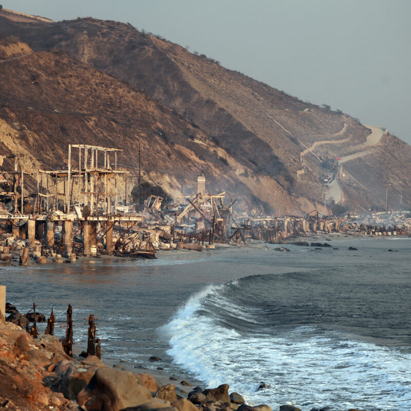 Coastal homes reduced to rubble on a scorched hillside overlooking the ocean.