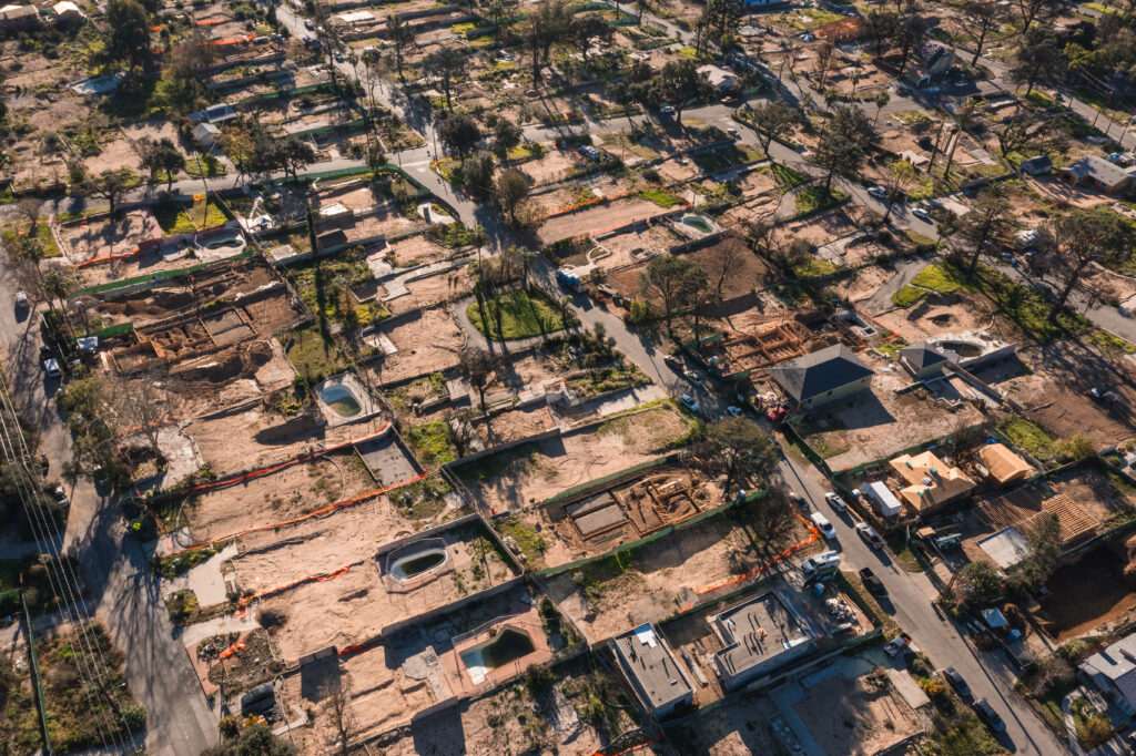 Aerial view of a residential neighborhood with numerous empty lots and partially constructed homes, surrounded by some existing houses, trees, and construction equipment.