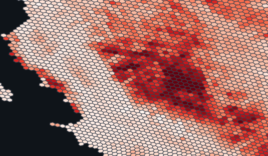 A hexagonal grid map with cells shaded from light pink to dark red, indicating varying data density. Darker red clusters are concentrated in the center-right, while the left side has mostly lighter cells and a black area.