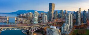 Aerial view of the Vancouver skyline at dusk, obscured by wildfire smoke, featuring the Granville Street Bridge spanning False Creek with mountains in the background.