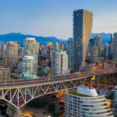 Aerial view of the Vancouver skyline at dusk, obscured by wildfire smoke, featuring the Granville Street Bridge spanning False Creek with mountains in the background.