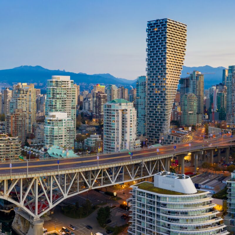 Aerial view of the Vancouver skyline at dusk, obscured by wildfire smoke, featuring the Granville Street Bridge spanning False Creek with mountains in the background.